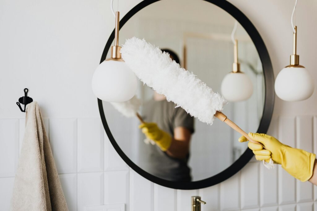 HOME 首頁 A person cleaning an elegant bathroom mirror with a fluffy duster and yellow gloves.