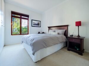 設備清潔 A stylish and comfortable bedroom interior featuring a wooden bed and nightstand with a red lamp and large window.