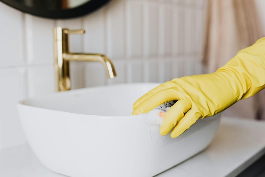 課程相關 Crop faceless person in yellow latex protective glove cleaning surface of white stylish sink in contemporary bathroom interior
