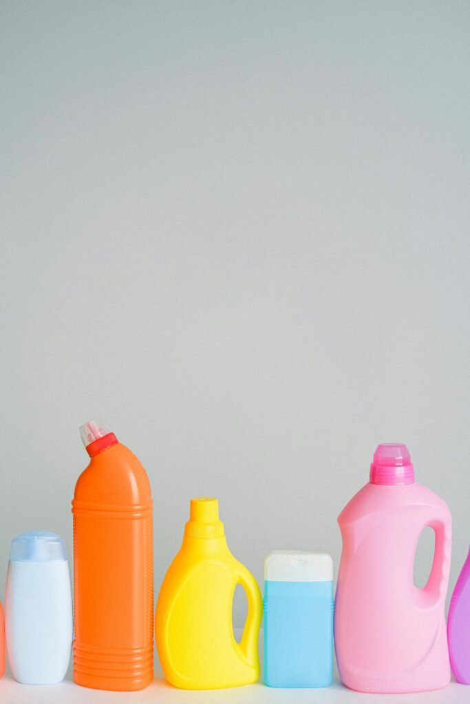 Set of assorted multicolored bottles with cleaning detergents for household routine placed on table against white wall in light room