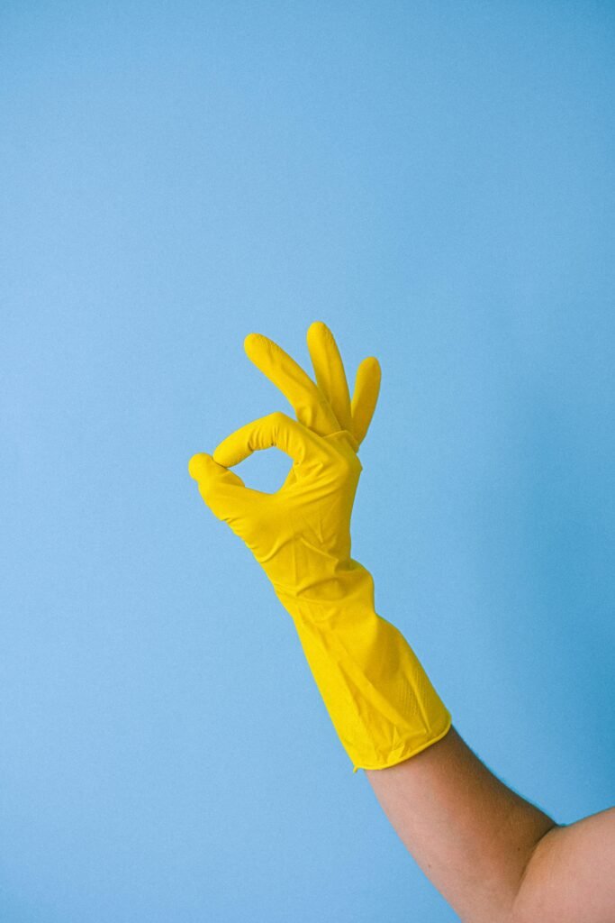 Yellow gloved hand making OK sign against a blue background, symbolizing approval.