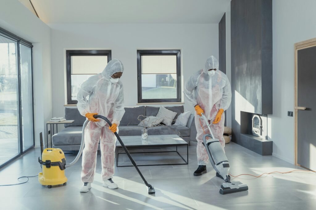 課程相關 Two workers in protective gear vacuum and disinfect a modern living room.