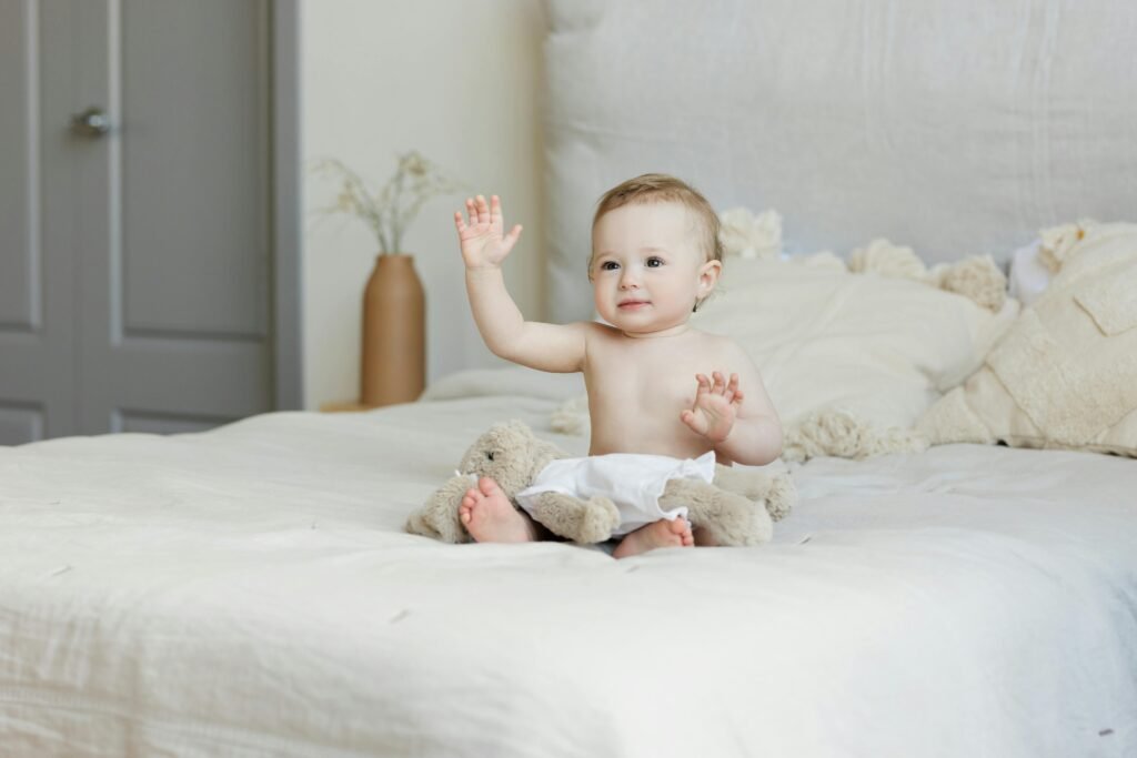 A cute baby happily sitting on a bed with plush toys, radiating a joyful expression.
