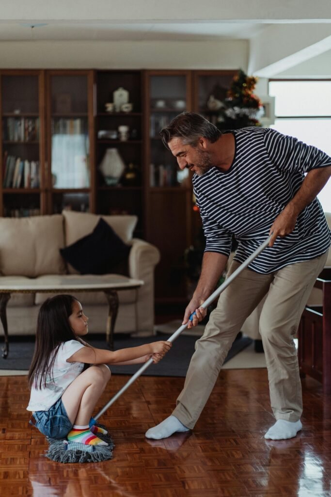 A father and daughter enjoying mopping the floor in the living room, having fun together.