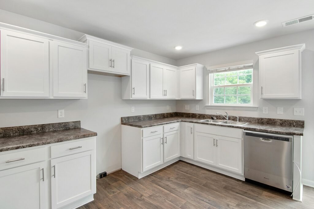 Spacious white kitchen featuring stainless steel appliances, white cabinets, and wood flooring.