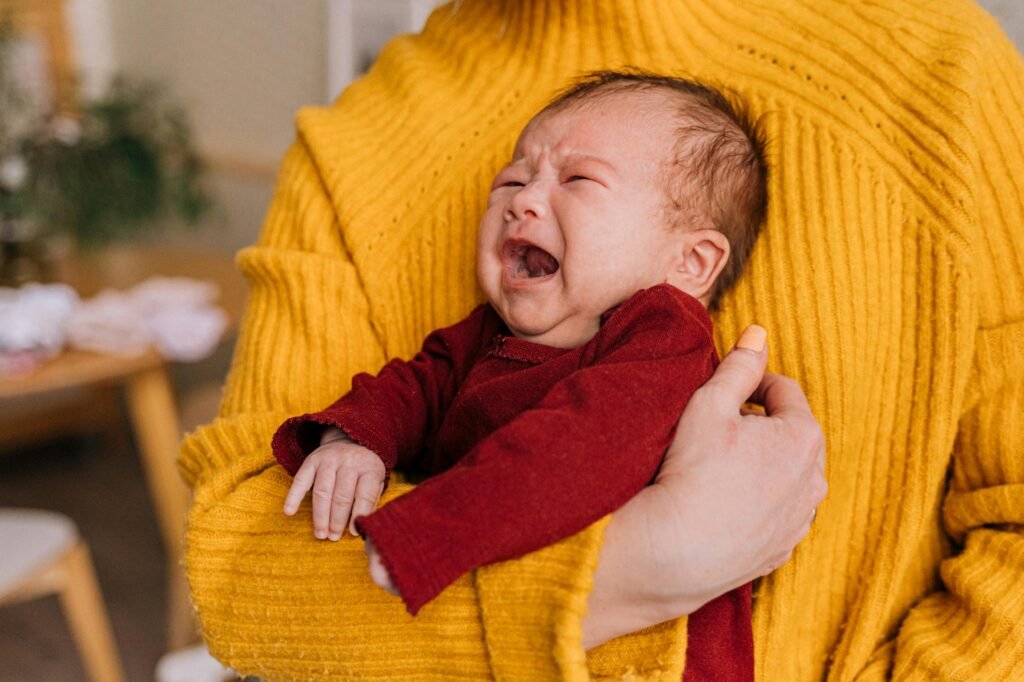 Emotional portrait of a crying newborn being comforted in caregiver's arms indoors.