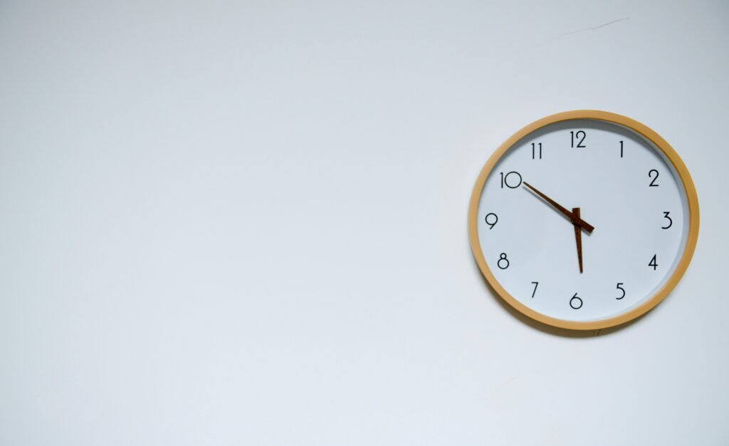 Simple wall clock with wooden frame against a white background, showing the time 10:10.