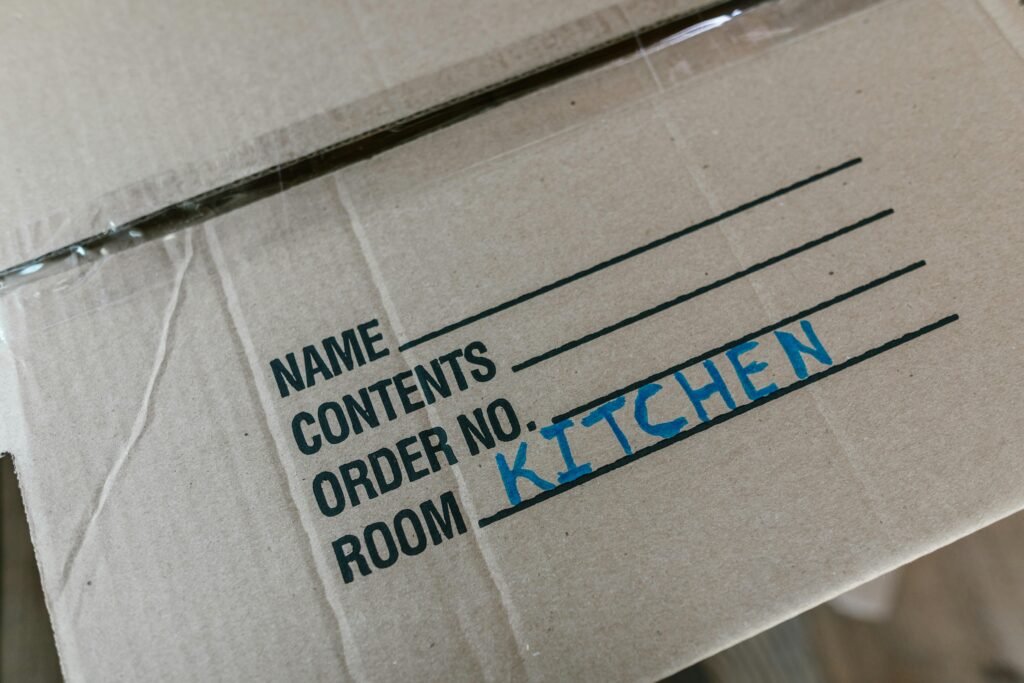 Cardboard box labeled with room destination for kitchen during moving process.