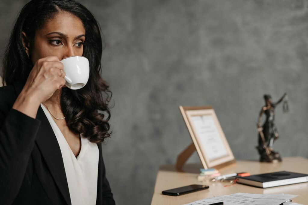 A focused professional woman drinks coffee at her desk in an office setting.