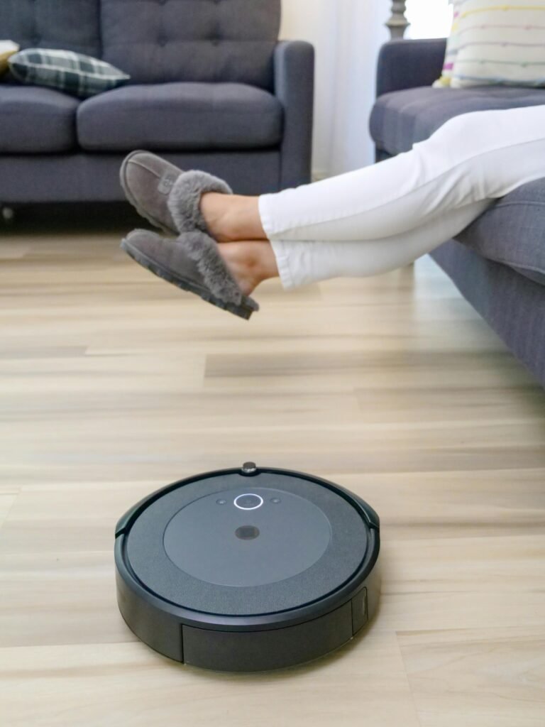 Autonomous robot vacuum cleaning hardwood floors under relaxing person's feet.