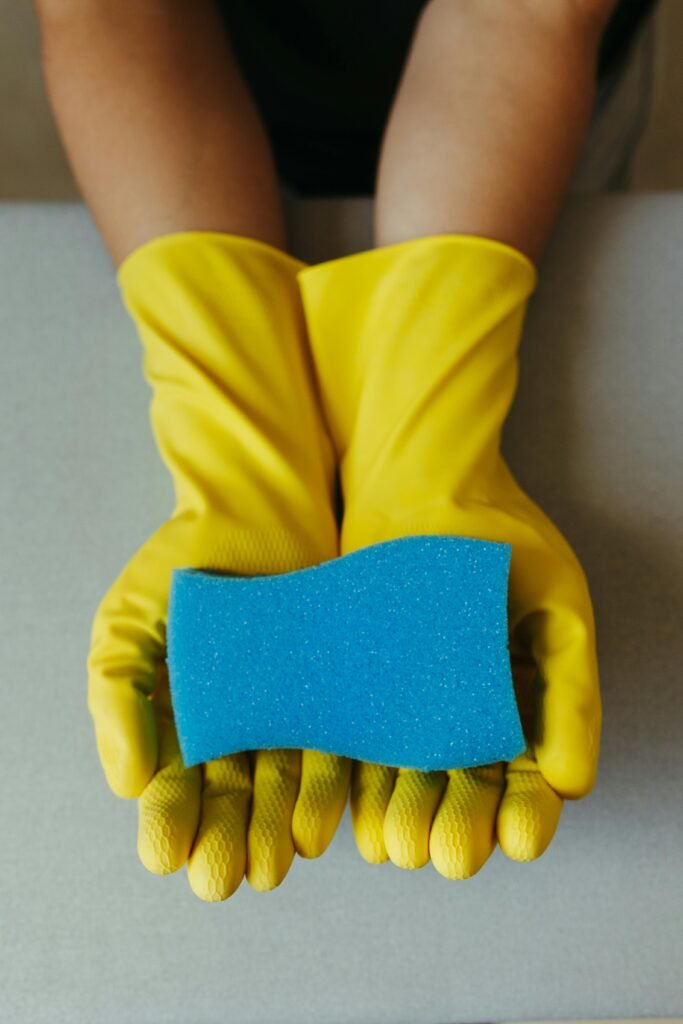 Close-up of yellow gloves holding a blue cleaning sponge, ideal for home cleaning themes.