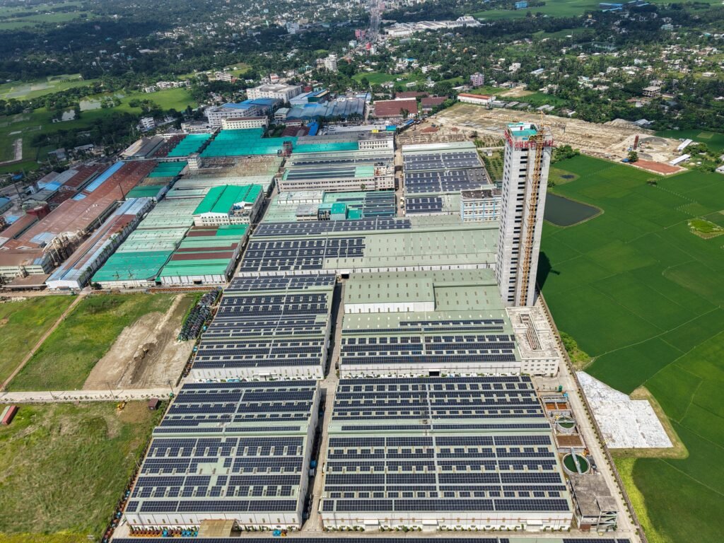 Sprawling industrial complex with solar panels and green fields, seen from above.
