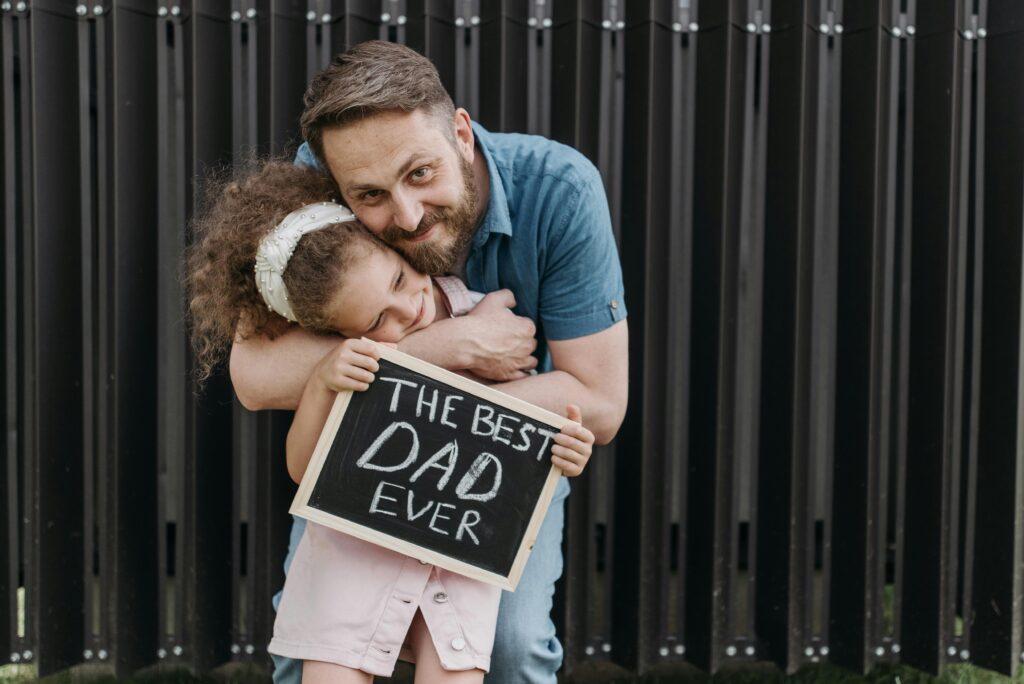 Father and daughter embrace with a sign saying 'The Best Dad Ever.'