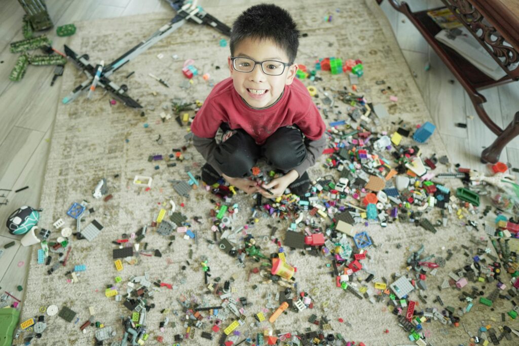 Young boy smiling while surrounded by colorful building blocks on a carpet indoors.